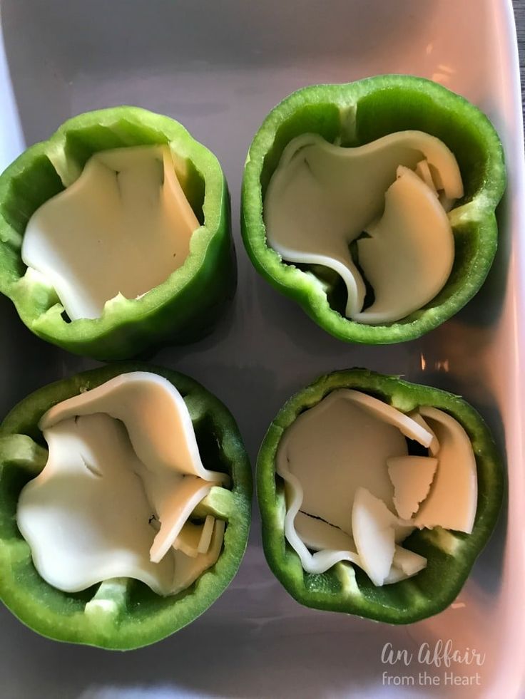 four green peppers with white sauce in them on a plate, ready to be eaten