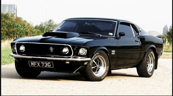 an old black muscle car is parked on the side of the road