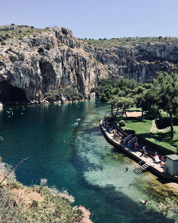 people are sitting on the edge of a boat in clear water near a rocky cliff