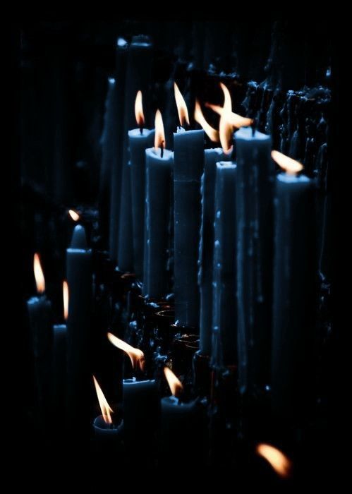 many lit candles are lined up in the dark