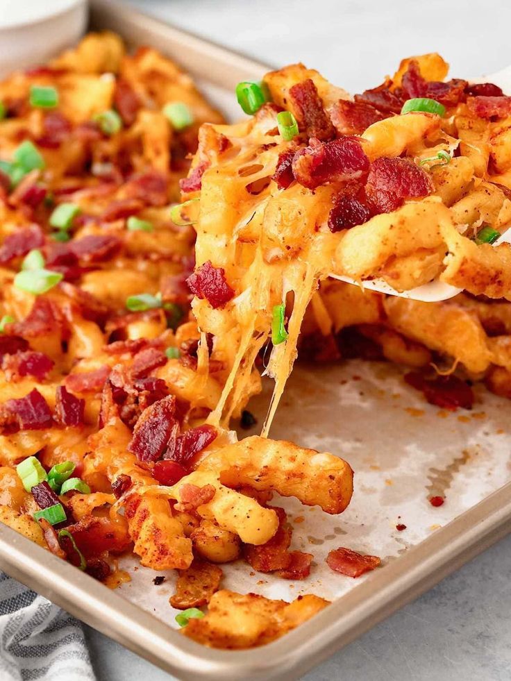 cheesy potato fries with bacon and green onions in a baking dish on a table