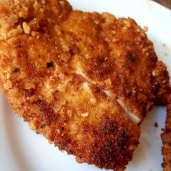 two pieces of fried chicken on a white plate with parmesan cheese and seasoning