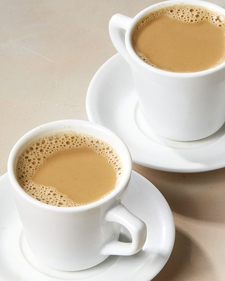 two white cups filled with liquid on top of a saucer next to each other