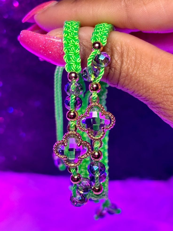 a woman's hand holding two bracelets with green beads and purple crystals on them