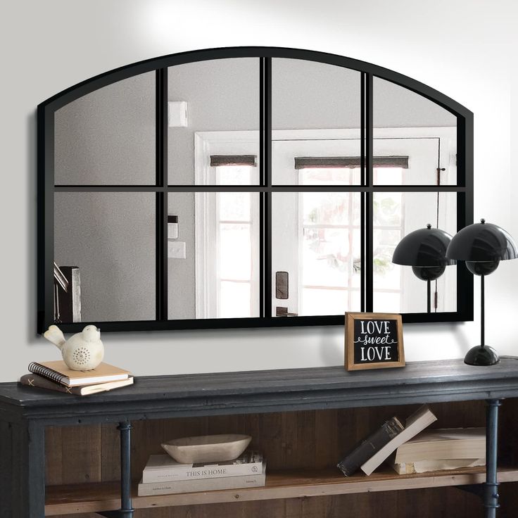 a large mirror on the wall above a table with books and lamp next to it