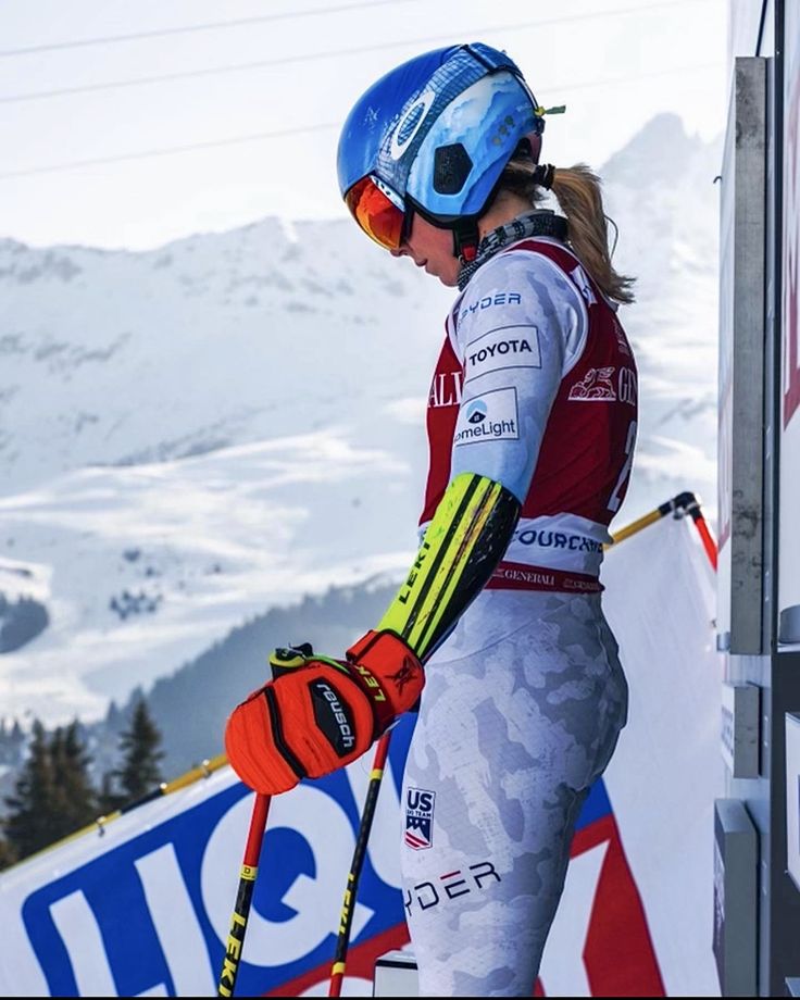 a woman in ski gear standing on the side of a snow covered slope with her skis