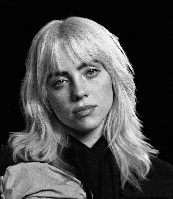 a black and white photo of a woman with blonde hair looking at the camera while wearing a jacket