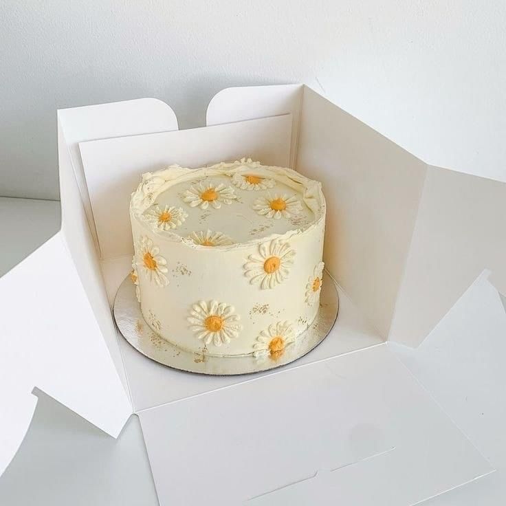 a white cake with yellow daisies on it in a card board box, ready to be cut