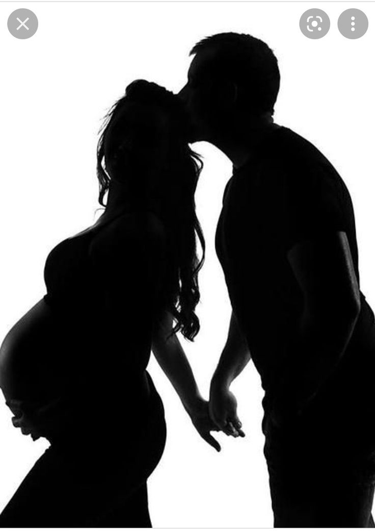 a pregnant couple kissing in silhouette against a white background