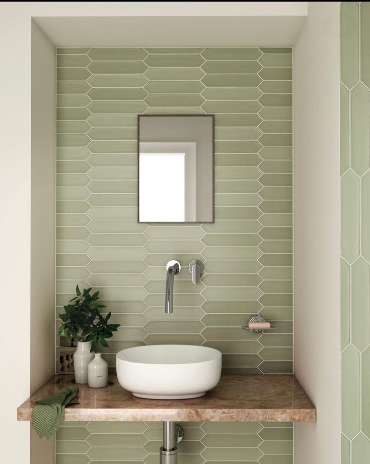 a bathroom with green tiles and a white bowl on the counter next to a mirror