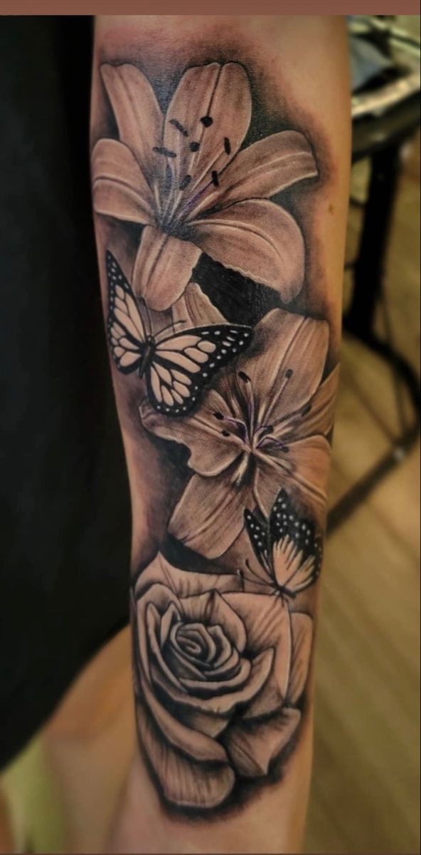 a black and white tattoo with flowers and butterflies on the arm, in front of a table