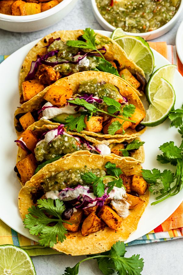 three tacos on a plate with cilantro, lime and guacamole