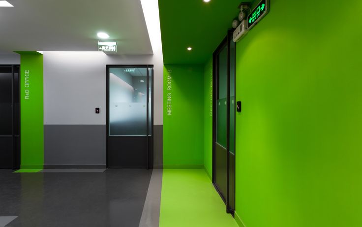 an empty hallway with green walls and black doors in the center is lit by recessed lights