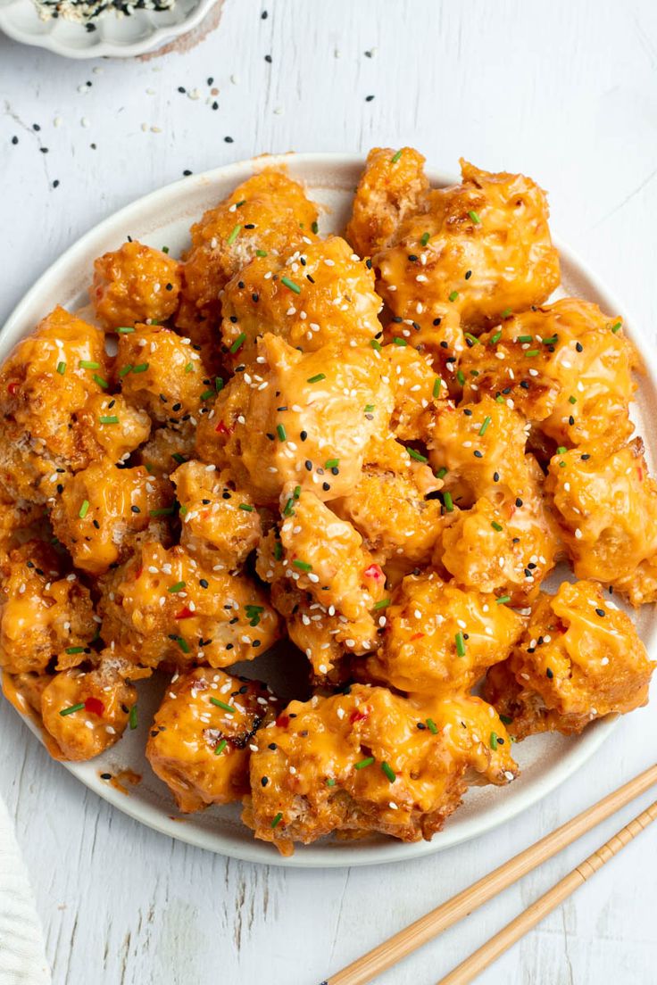 a white plate topped with chicken covered in sesame seeds and seasoning next to chopsticks