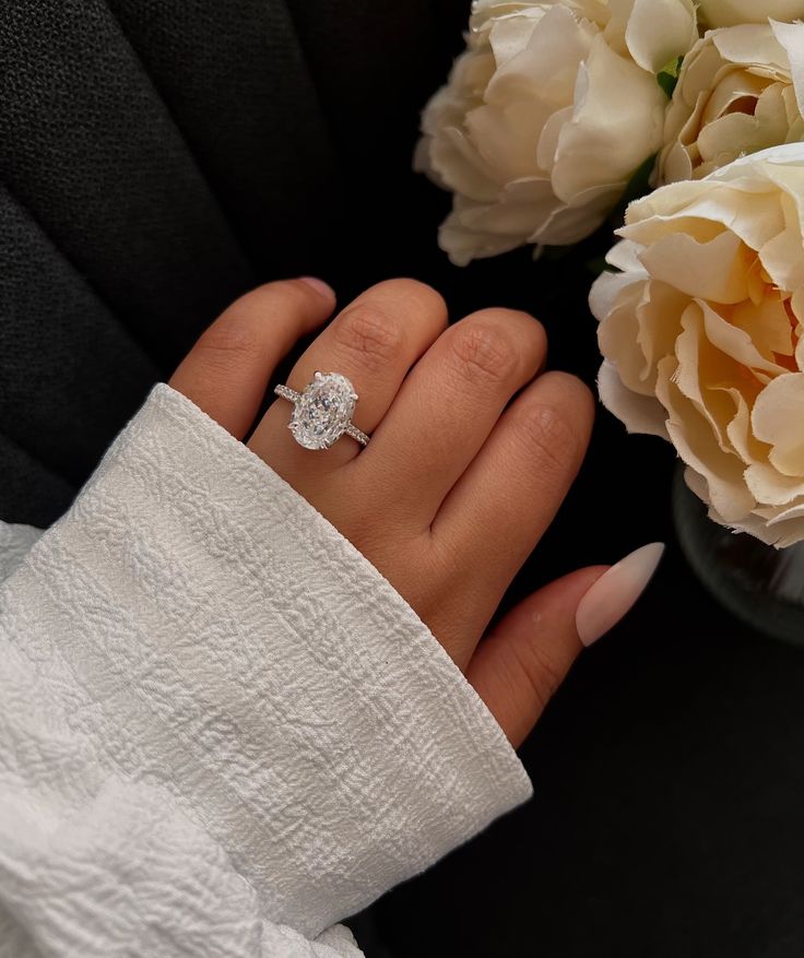 a woman's hand with a diamond ring on it next to some white flowers