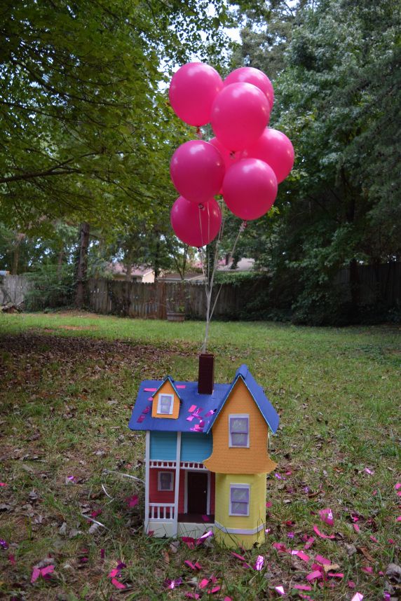 a toy house with balloons attached to it in the middle of some grass and pink flowers