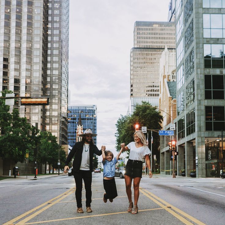 a man, woman and child crossing the street in front of tall buildings on a cloudy day