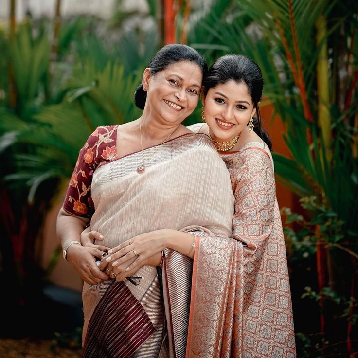 two women standing next to each other in front of trees and plants, one holding the other