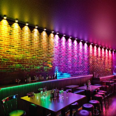 an empty restaurant with colorful lights on the brick wall and tables in front of it