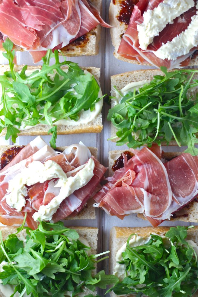 several sandwiches with meat, cheese and arugula sprouts on them are arranged in rows