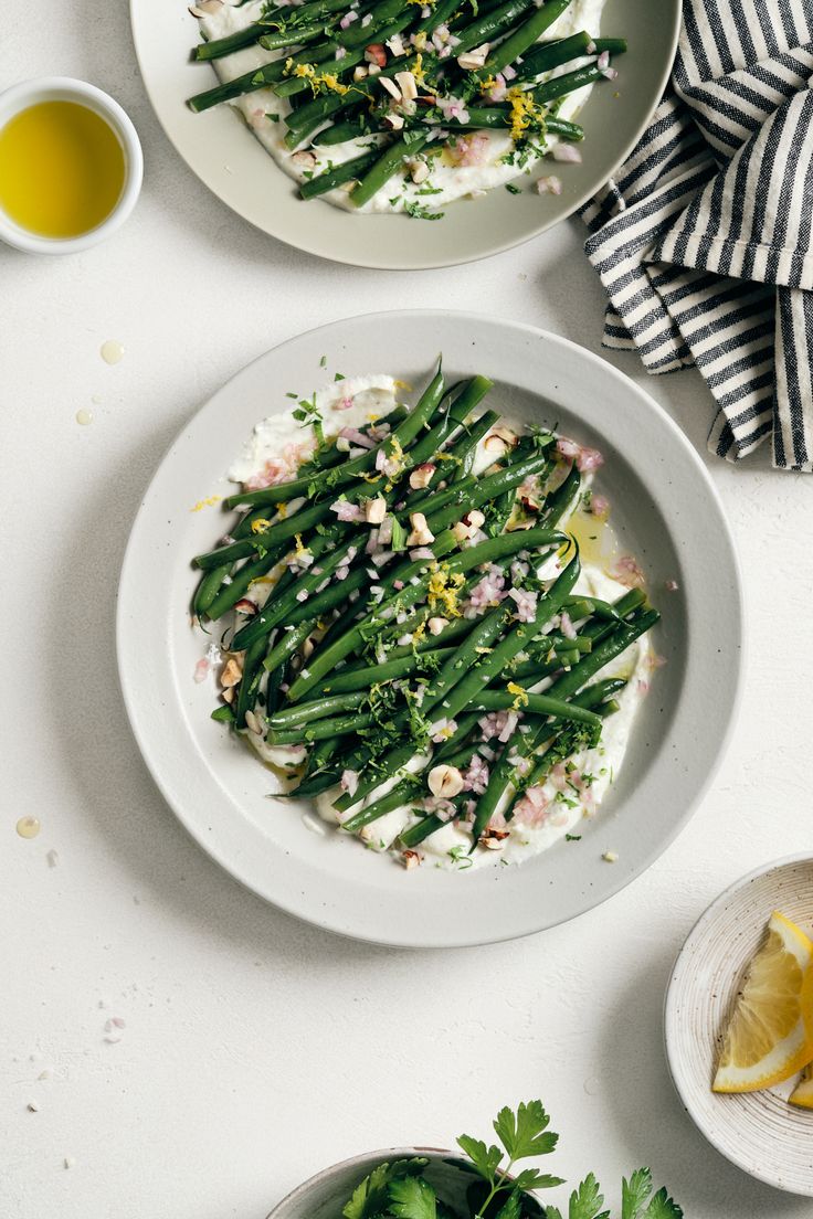 two plates filled with green beans and other food on top of a white tablecloth