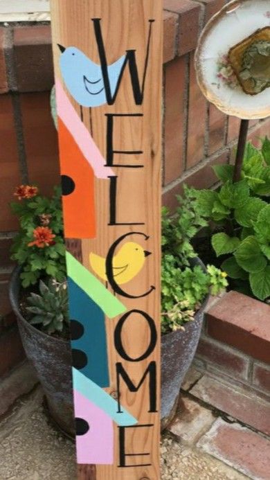 a wooden welcome sign sitting next to a potted plant