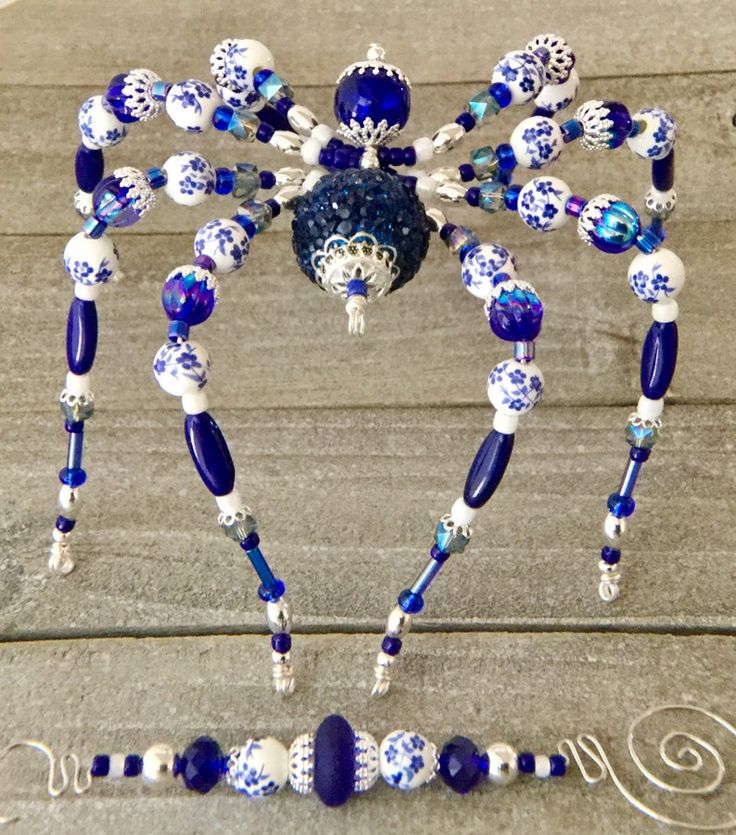 a blue and white spider made out of glass beads on a wooden surface with the word love spelled below it