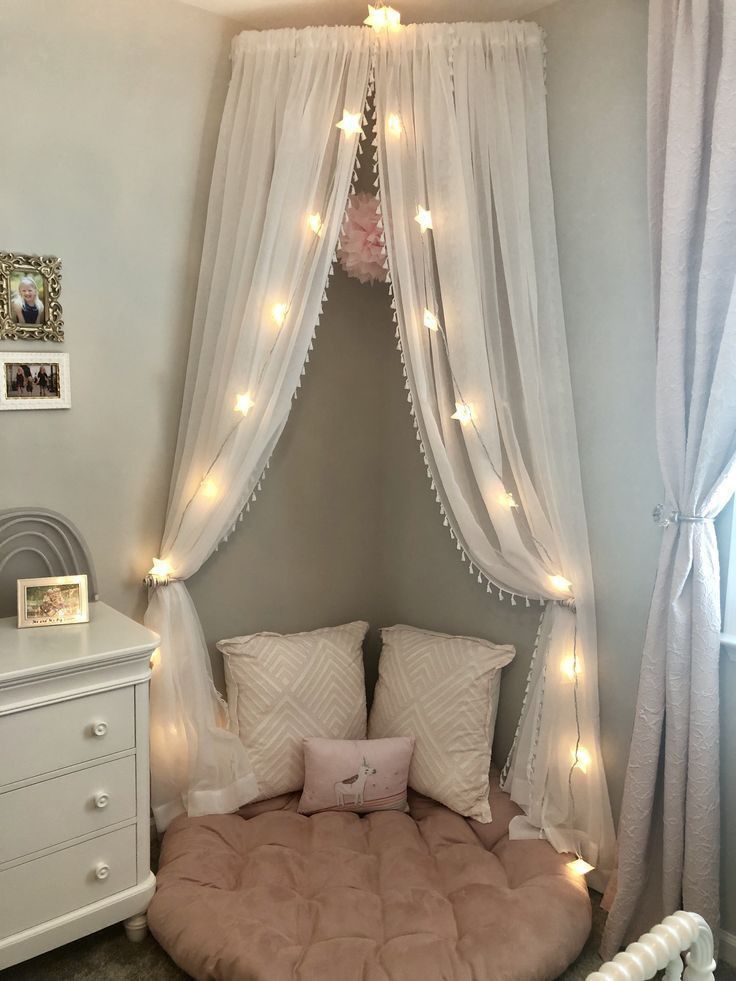 a bed with white curtains and lights hanging from the ceiling