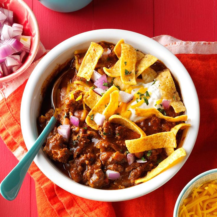 a bowl filled with chili and tortilla chips next to two bowls of shredded cheese