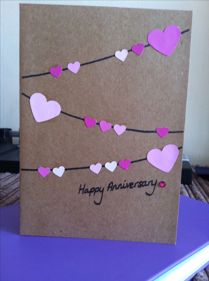 a brown card with pink and white hearts hanging on a line that says happy anniversary