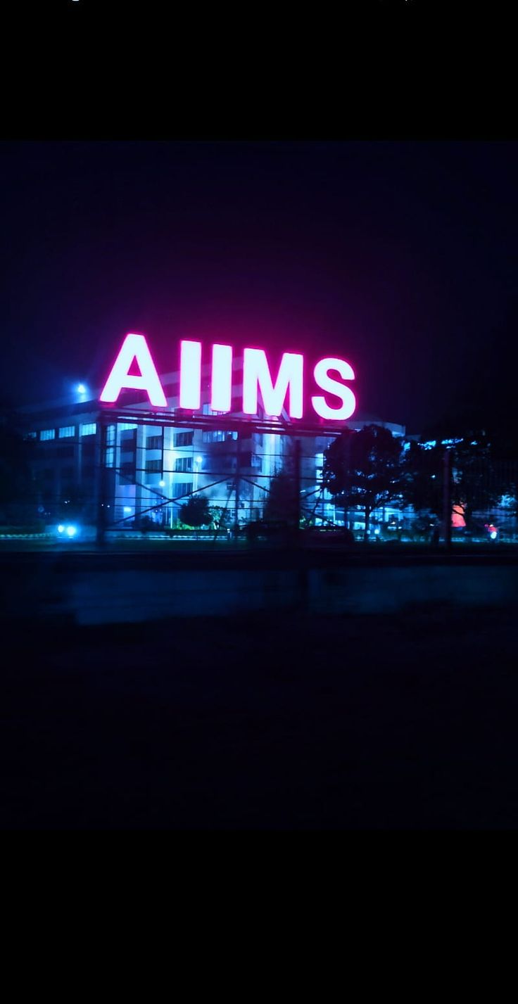 an illuminated sign that says aims in front of a building with lights on it at night