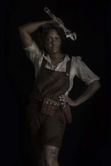 a woman in overalls holding a pair of scissors on her head with both hands