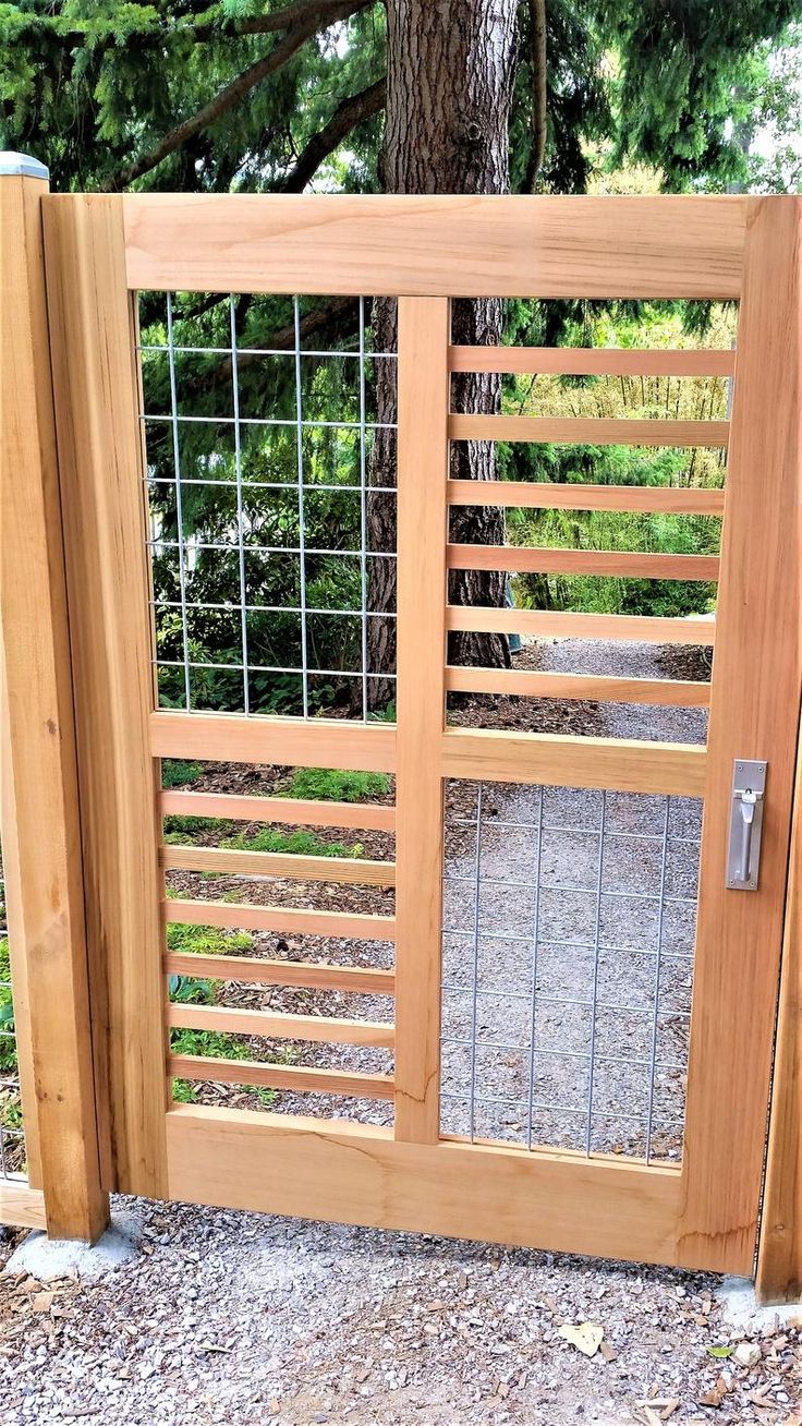 an open wooden gate with metal bars on the top and bottom panels, in front of a tree