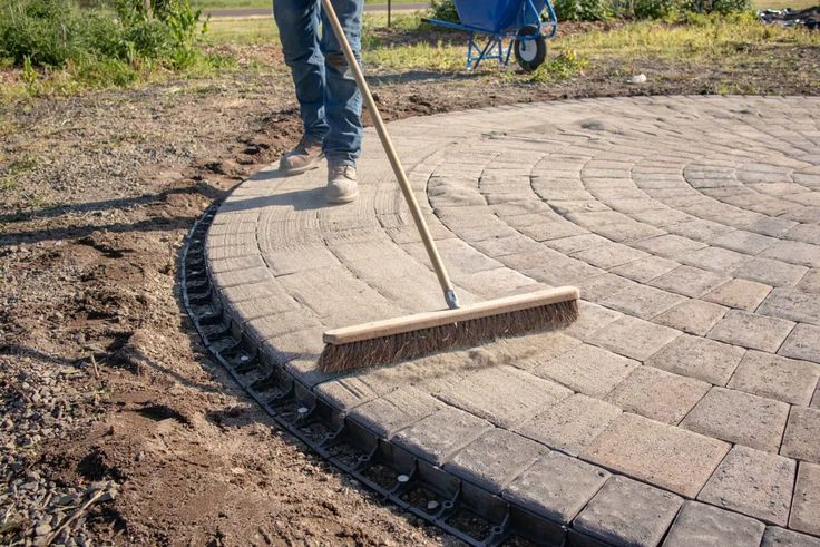 a person with a broom is standing on a brick walkway in the middle of a garden