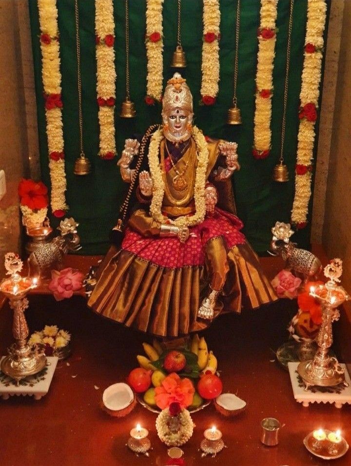 an idol is sitting on a table with candles and flowers around it in front of a green backdrop