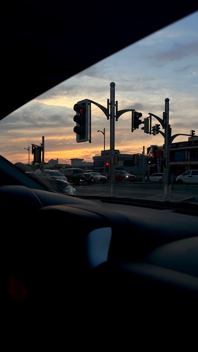 the sun is setting behind some traffic lights and cars are driving down the street in front of them