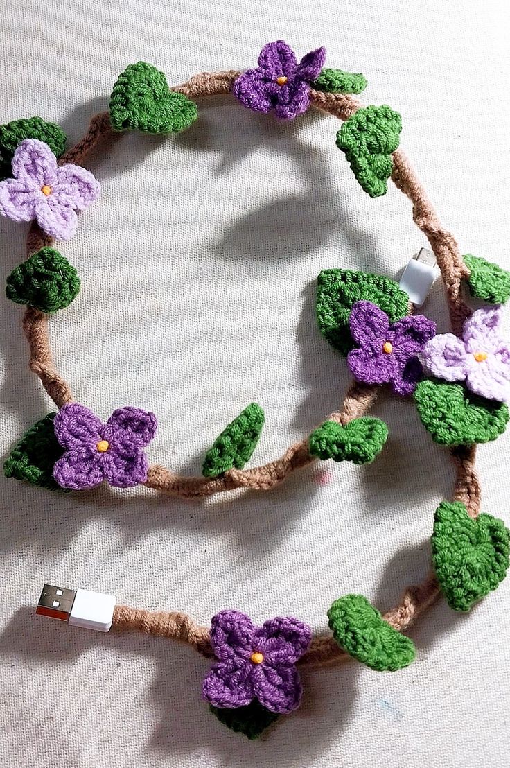 a crocheted cell phone strap with flowers and leaves attached to the end, sitting on a white surface