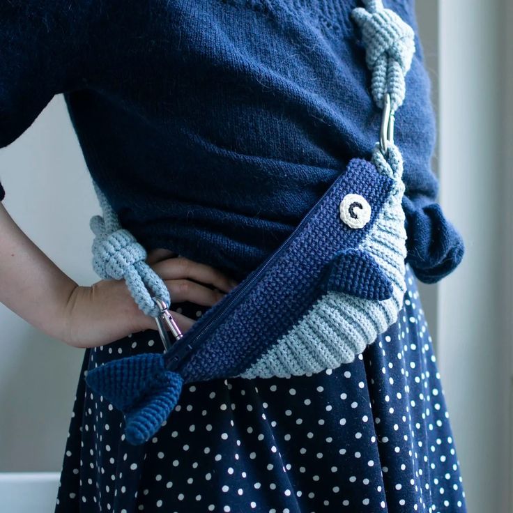 a woman wearing a blue sweater and polka dot skirt holding a knitted owl purse