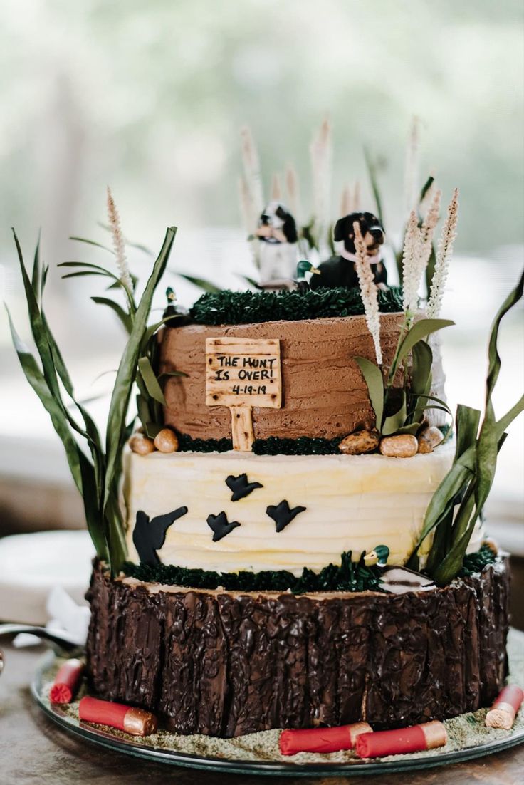 a three tiered cake is decorated with grass and flowers on the top, along with a wooden sign