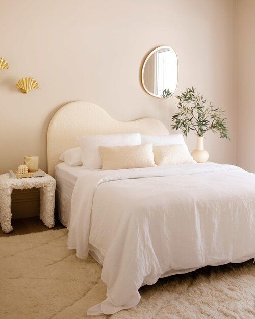 a white bed sitting in a bedroom next to a table with a mirror on it