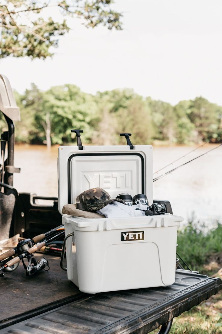 a white cooler sitting on top of a truck with fishing gear in it's back