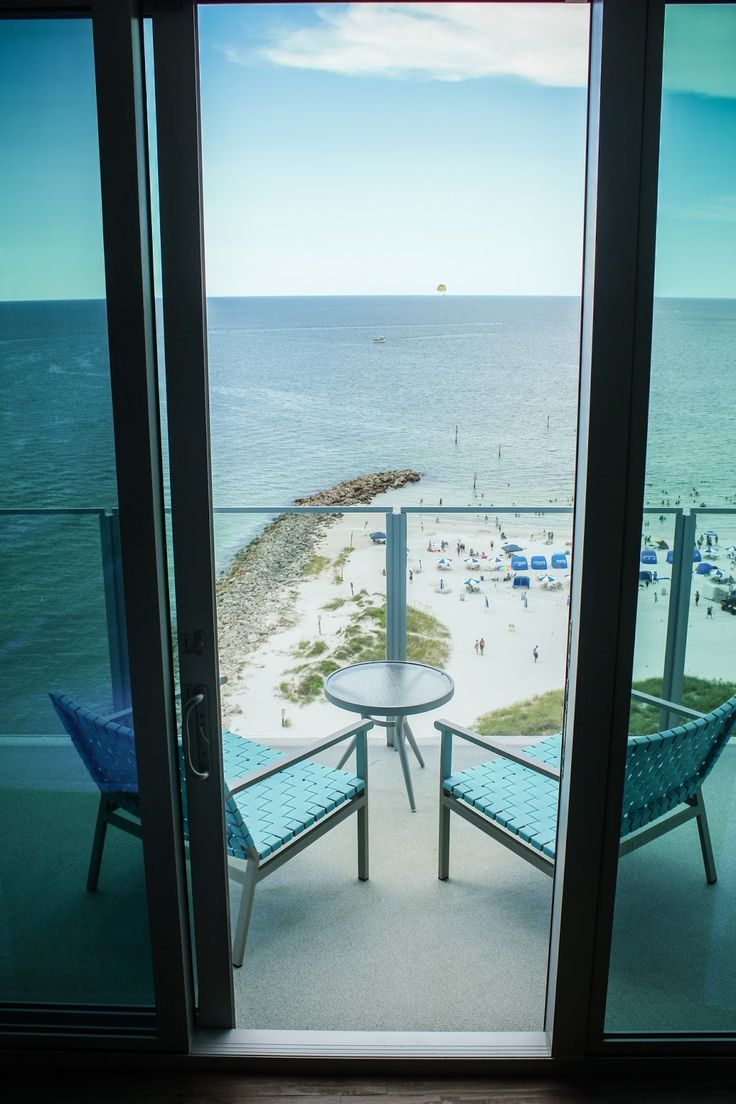 an open door to a balcony with chairs and tables overlooking the beach in front of it