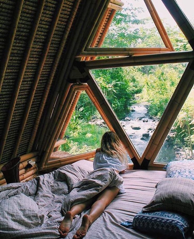 a woman laying on top of a bed in a room filled with wooden walls and windows