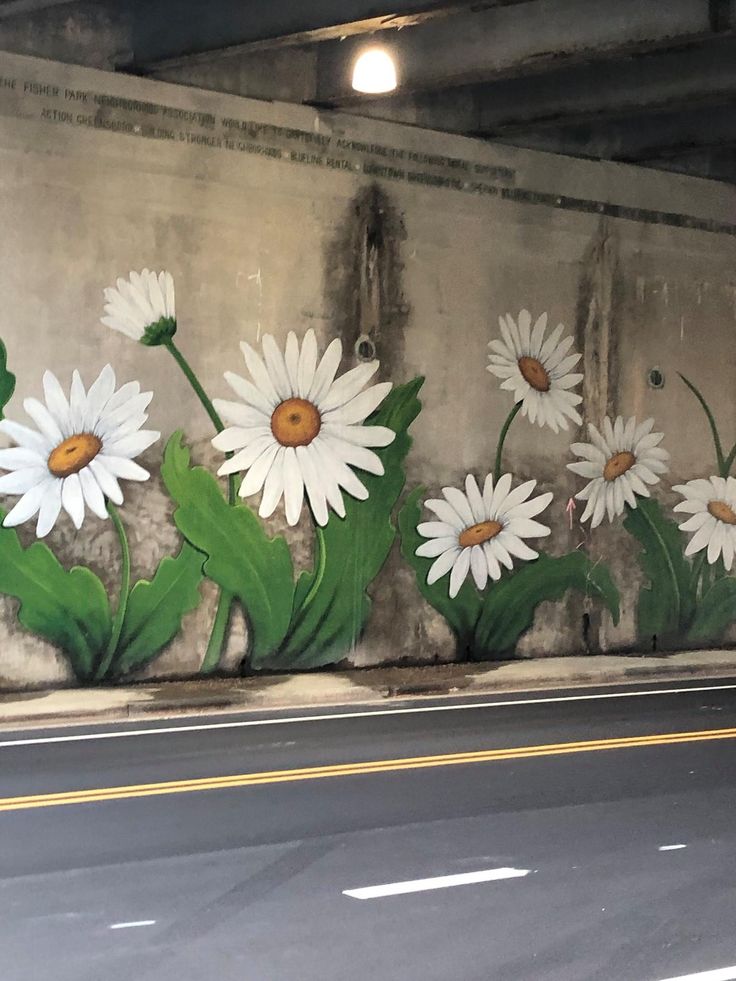 some white daisies painted on the side of a concrete wall next to a street