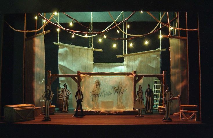 the stage is set up for a play with lights strung over it and curtained walls