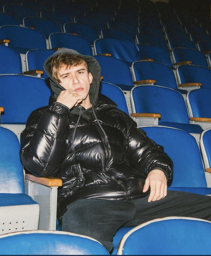 a young man sitting in an empty auditorium with his hand on his chin and looking at the camera