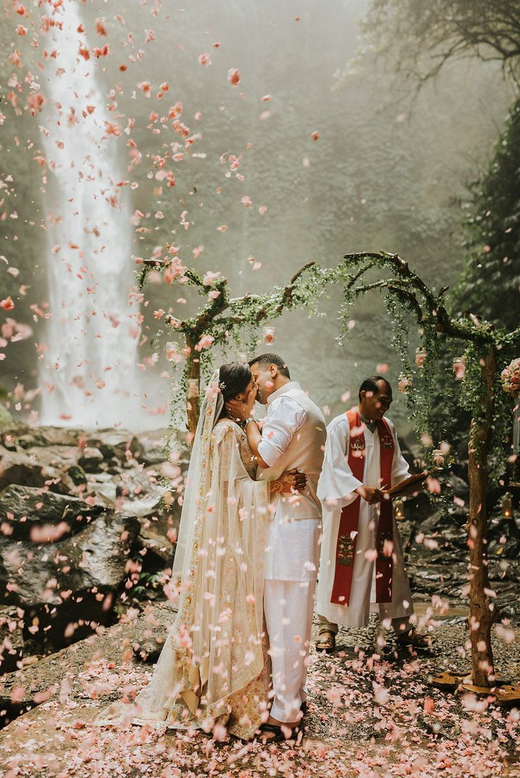 a bride and groom kissing in front of a waterfall surrounded by petals at their wedding