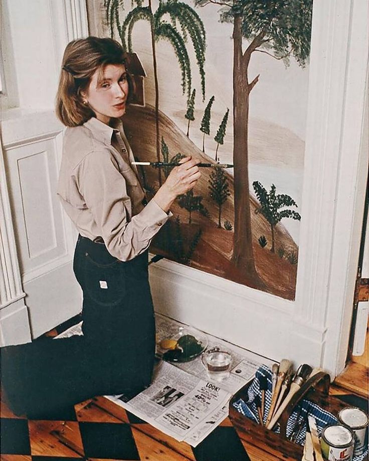 a woman sitting on the floor in front of a painting with trees and animals painted on it