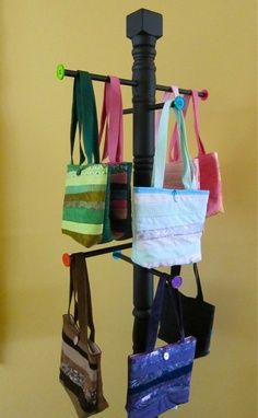 several purses are hanging from a coat rack on a pole in front of a yellow wall