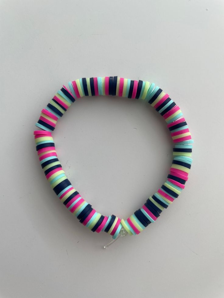 a bracelet with multicolored stripes on it sitting on a white table next to a silver hook